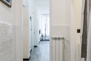 A hallway with white tiled walls, a radiator, and a door leading to a room. - [Aquarium 5']Free Wifi & Netflix Prion by TILO (Genoa)