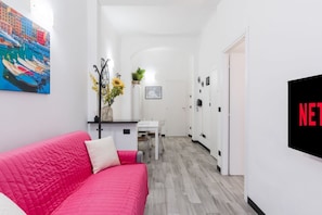 A modern hotel room with a pink bed, a dining area, and a TV screen displaying the Netflix logo. - [Aquarium 5']Free Wifi & Netflix Prion by TILO (Genoa)