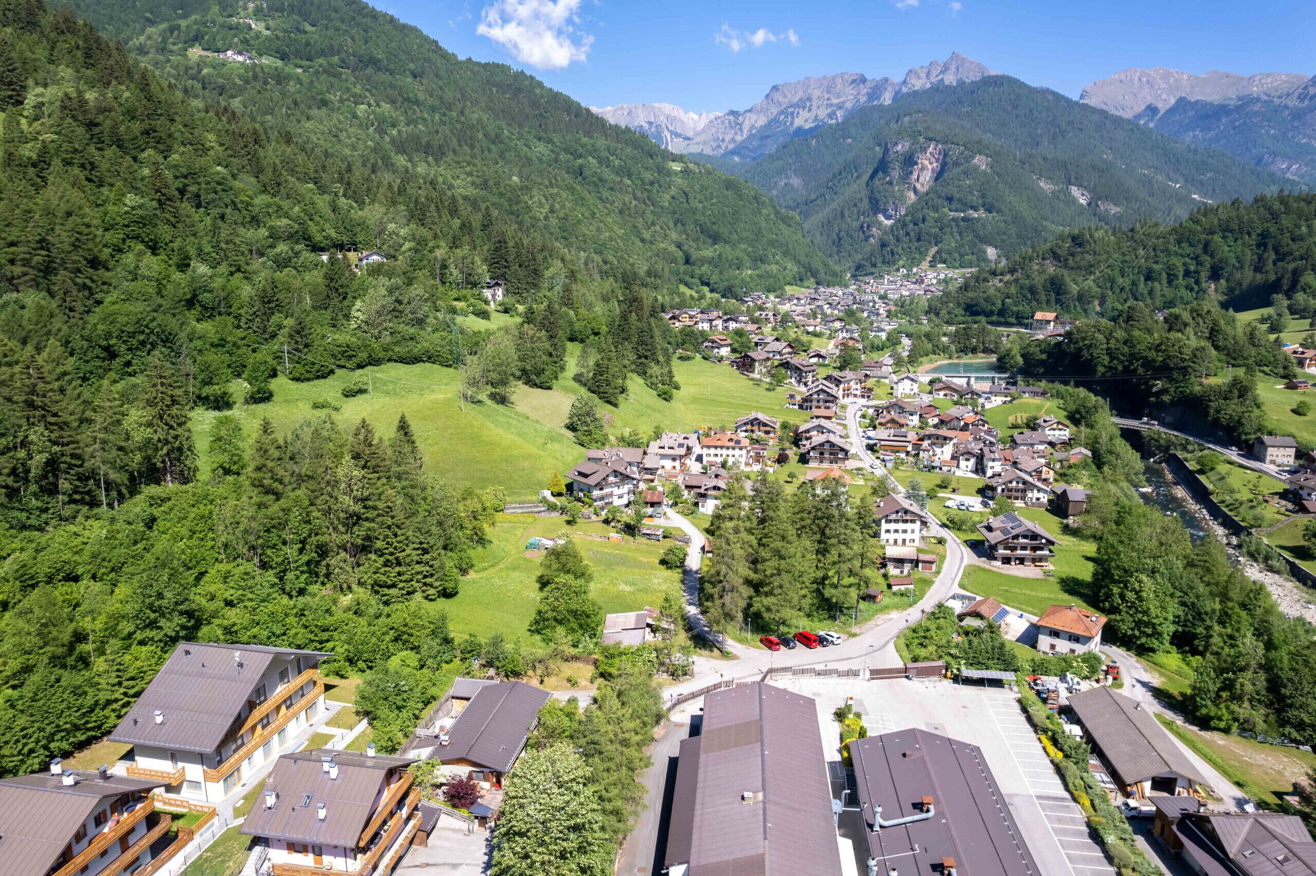 A mountainous village with traditional houses, a central road, and a small body of water.