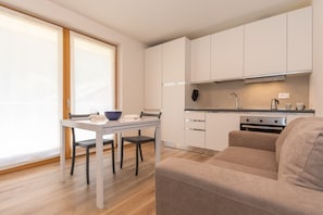 Een moderne keuken met witte kasten, een eettafel met stoelen, een bank en een groot raam.
