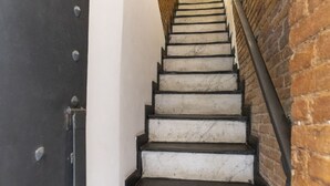 Una escalera con escalones blancos y bordes negros, que lleva a una puerta de madera con remaches metálicos.