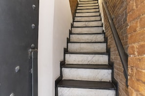 Eine Treppe mit weißen Stufen und schwarzen Kanten, die zu einer Holztür mit Metallnieten führt.