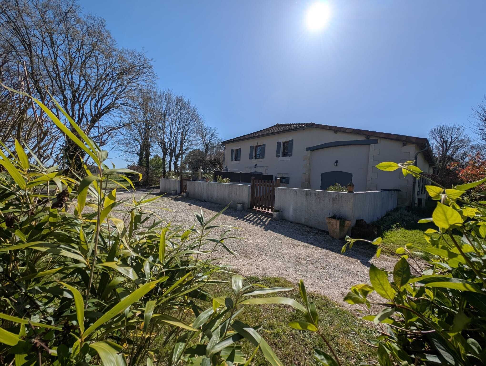 Une maison avec une allée en gravier, un portail en bois et un ciel d’un bleu éclatant.