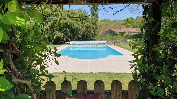 A swimming pool with a wooden deck, surrounded by greenery and a wooden fence. - Domaine Bardon (Chaunac)
