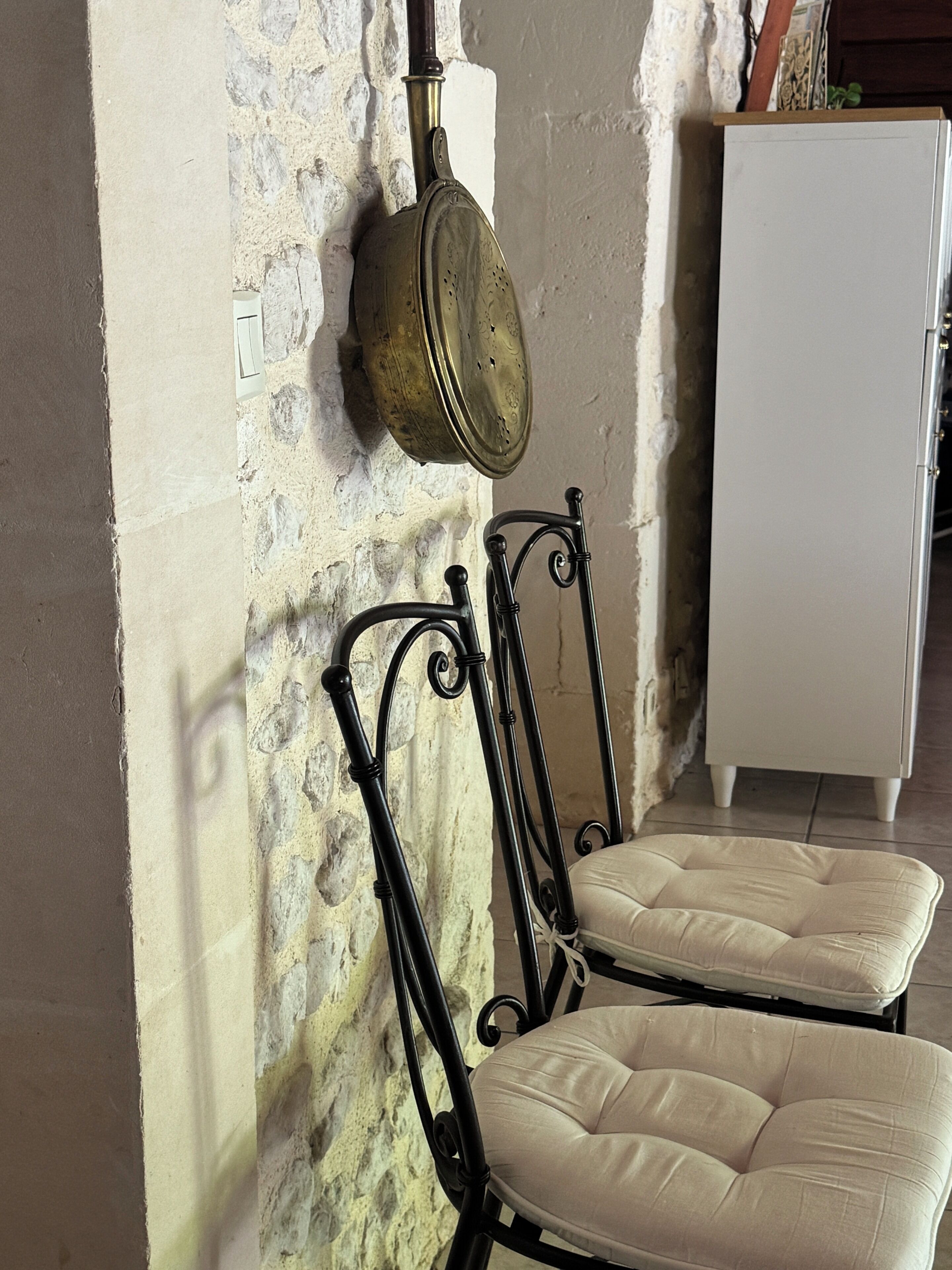 A room with a stone wall, a metal-framed chair with a cushion, and a white cabinet.