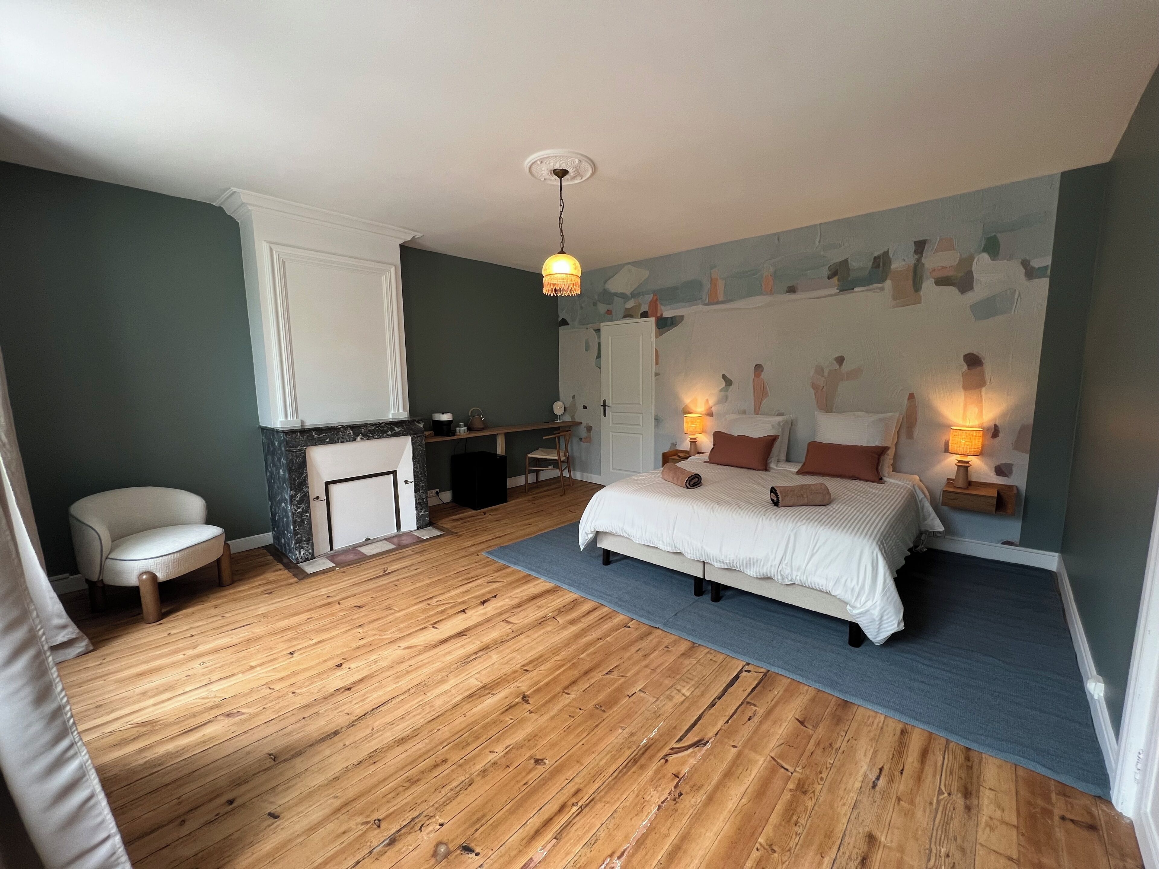 Une chambre à coucher avec un lit, des lampes de chevet, une chaise, un bureau et une cheminée.
