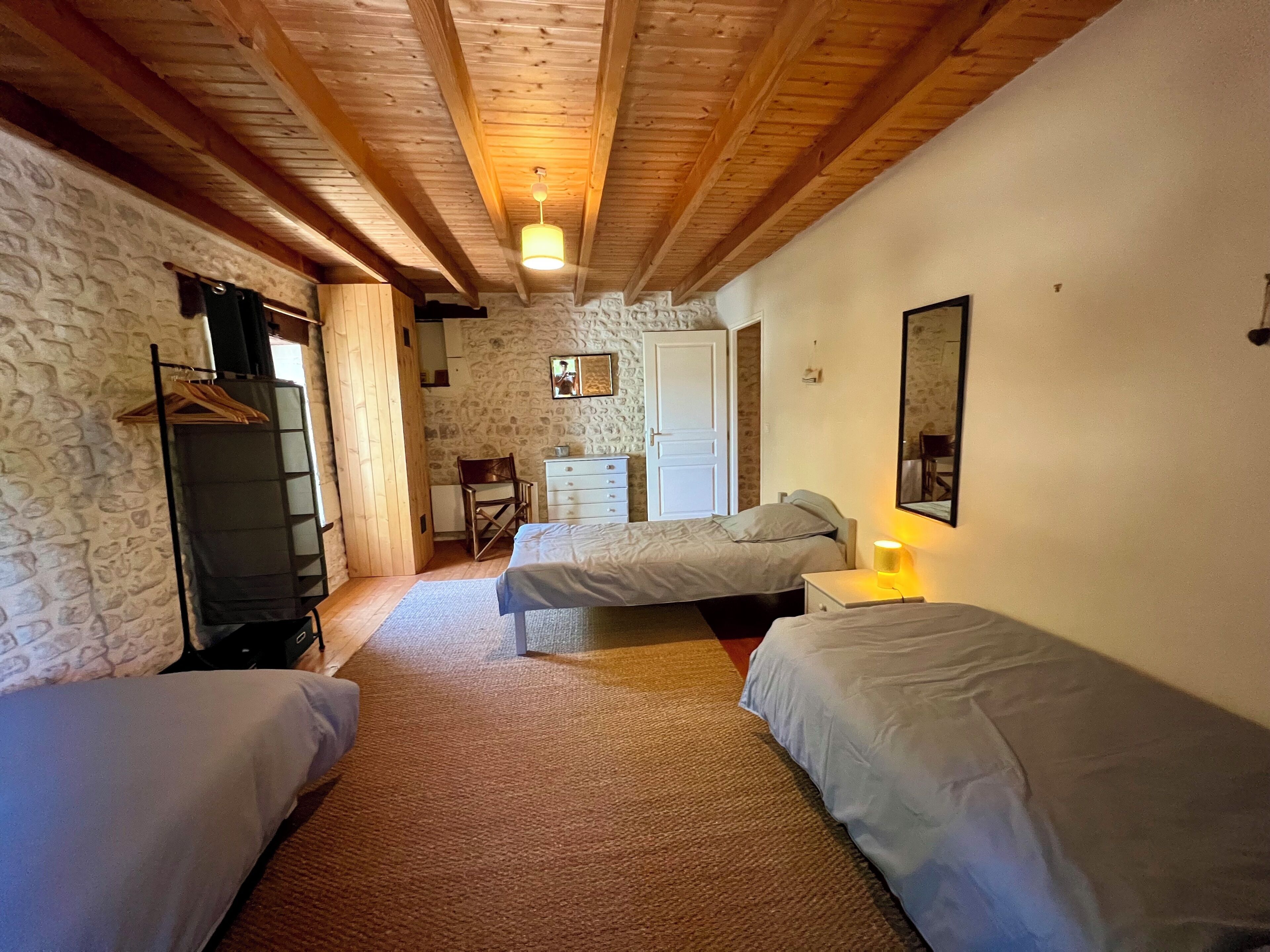 Una habitación con dos camas, techo de madera, pared de piedra, cómoda, silla y espejo.