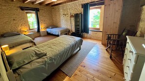 A rustic bedroom with two beds, a dresser, a chair, and a stone wall. - Domaine Bardon (Chaunac)