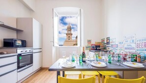 A modern kitchen with a built-in microwave, oven, and a dining area with yellow chairs. A window reveals a view of a tower. - City Center, Free Wifi & Netflix By Tilo (Genoa)