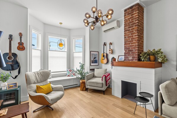 A living room with a fireplace, a large window, and a guitar wall. - Heritage Glam Home BBQ + Patio Parking DT (St. John's)