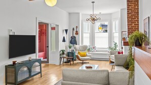 A modern living room with a flat-screen TV, a sofa, a coffee table, and a dining area with a bench. - Heritage Glam Home BBQ + Patio Parking DT (St. John's)