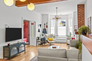 A modern living room with a flat-screen TV, a sofa, a coffee table, and a dining area with a bench. - Heritage Glam Home BBQ + Patio Parking DT (St. John's)
