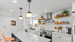 A modern kitchen with marble countertops, stainless steel appliances, and wooden shelves with plants. - Heritage Glam Home BBQ + Patio Parking DT (St. John's)