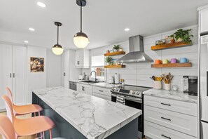 A modern kitchen with marble countertops, stainless steel appliances, and wooden shelves with plants. - Heritage Glam Home BBQ + Patio Parking DT (St. John's)