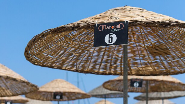 Sillas de playa y sombrillas de paja con un cartel que indica un número de suite.