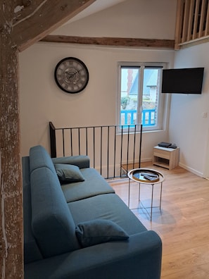 A living room with a sofa, a clock, a TV, and a window with a view. - Hyper-center - Beach on foot - Cosy accommodation (Villers-sur-Mer)