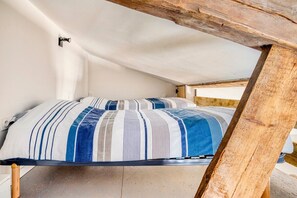 Cama em quarto estilo loft com teto inclinado e vigas de madeira aparentes.