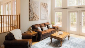 Ein geräumiges Wohnzimmer mit großem Fenster, einem braunen Ledersofa, einem Holztisch und einem gemusterten Teppich.