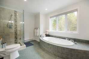 Une salle de bain dotée d’une douche à parois de verre, d’une baignoire sur pieds et d’une fenêtre laissant entrer la lumière naturelle.