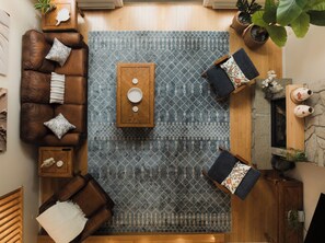 A room with a brown leather sofa, a patterned rug, a wooden coffee table, and a stone fireplace. - Birch Grove Chalet, Hot Tub, Golf, Private Forest (Humber Valley Resort)