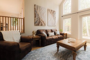 Un salon avec un canapé en cuir marron, une table basse en bois et des œuvres d’art abstraites accrochées au mur.