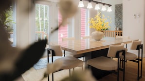 Ein moderner Essbereich mit einem Glastisch, mehreren Stühlen, einer Vase mit gelben Blumen und einer Wand aus Naturstein.