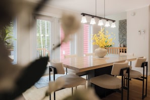 A modern dining area with a glass table, multiple chairs, a vase with yellow flowers, and a stone accent wall.