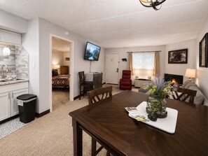 Ein modernes Wohnzimmer mit Kamin, Esstisch mit Stühlen, Küchenzeile und Wandfernseher.