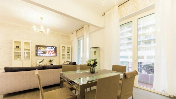 Una sala moderna con un sofá, una mesa de comedor con superficie de vidrio y un televisor.