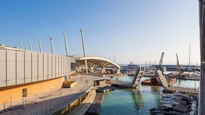 Un porto turistico con barche, un edificio di grandi dimensioni con tetto curvo e un ponte che collega al molo.