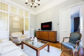A living room with a sofa, armchair, coffee table, and a television displaying 'NETFLIX'. - Beach | 2BR| Luxury Genoa| Wifi By Tilo (Genoa)