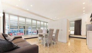 A modern living room with a sofa, dining table, chairs, and large windows offering a view of the city. - Aquarium View | 4 People | AC | WIFI By Tilo (Genoa)
