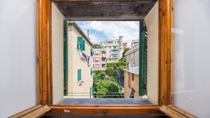 A view through a window with a wooden frame, looking at a narrow street with buildings and greenery. - Bocadasse Beach| Parking| Wifi| By Tilo (Genoa)