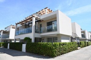 Un edificio residencial moderno de dos pisos con balcón, pérgola y escalera.