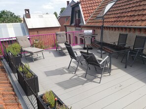 Eine Dachterrasse mit Gartenmöbeln, einem Grill und Blick auf die Nachbarschaft.