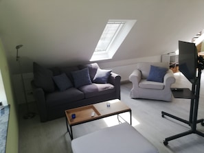 Un salon comprenant un canapé, un fauteuil et une petite table sur laquelle se trouve une télécommande.