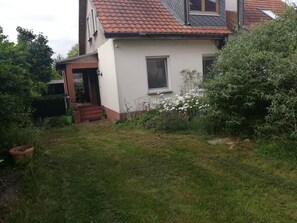 Een huis met een rood pannendak, een witte gevel en een kleine voortuin met gras en planten.