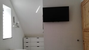 A room with a flat-screen TV mounted on the wall, a white dresser, a bench, and a wooden door. - Quiet apartment with very large roof terrace (Wittenburg)