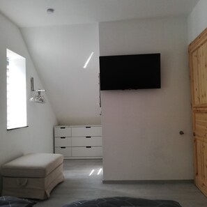 A room with a flat-screen TV mounted on the wall, a white dresser, a bench, and a wooden door. - Quiet apartment with very large roof terrace (Wittenburg)
