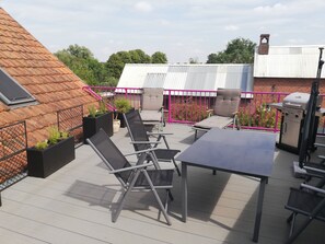 Een terras op het dak met een tafel, stoelen, een barbecue en potplanten.