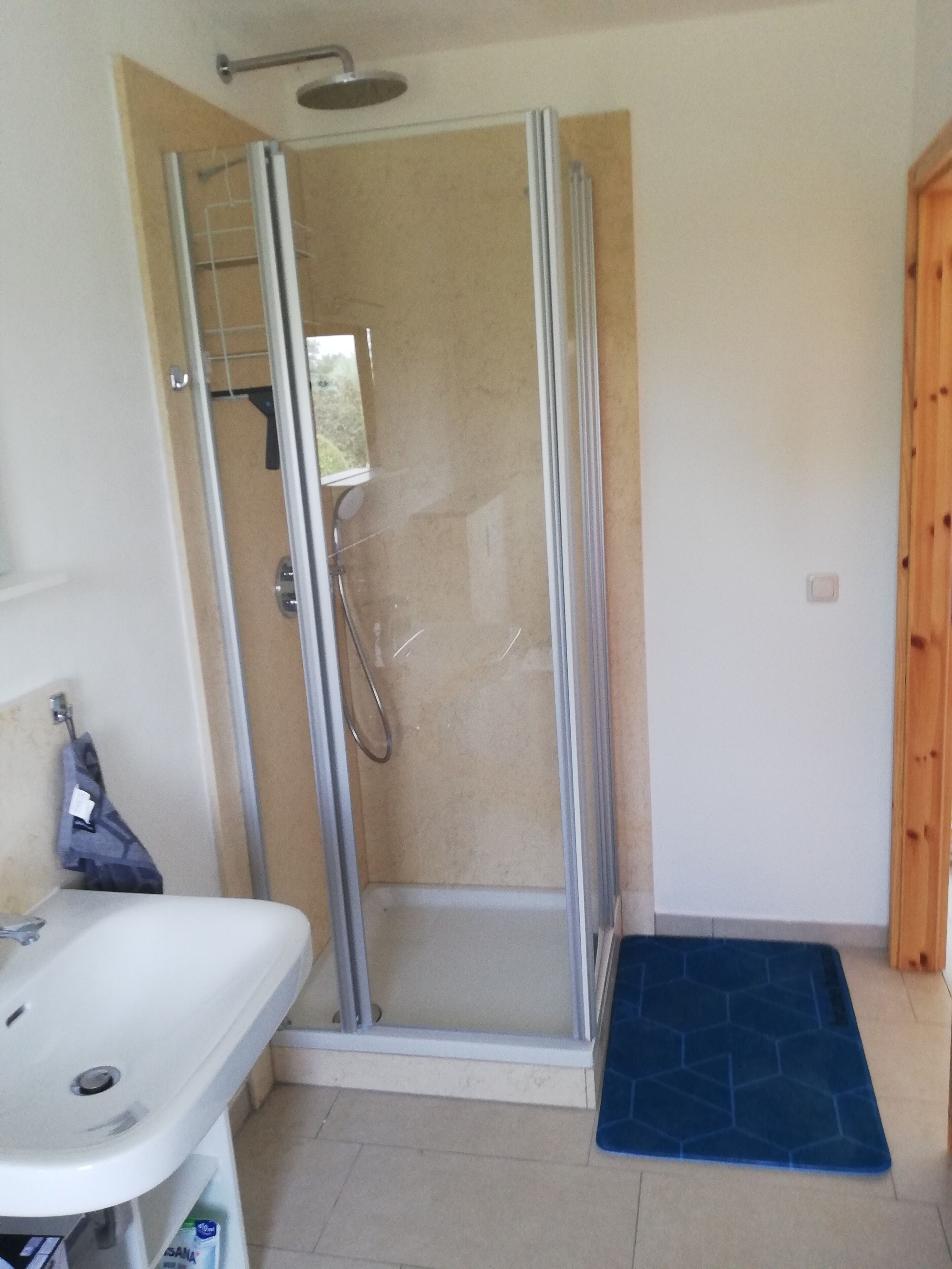 A shower with a glass door, a sink, and a blue mat.