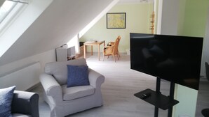 An attic room with a TV, a sofa, a dining table with chairs, and a map on the wall. - Quiet apartment with very large roof terrace (Wittenburg)