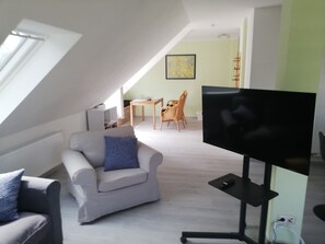 An attic room with a TV, a sofa, a dining table with chairs, and a map on the wall. - Quiet apartment with very large roof terrace (Wittenburg)