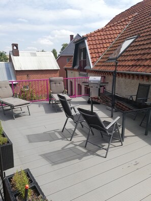 Een dakterras met buitenmeubilair, een barbecue en uitzicht op omliggende gebouwen.
