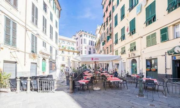 A street with outdoor seating, buildings with shutters, and a cafe sign. - Aquarium 5'| 1BR | A/C| By Tilo (Genoa)