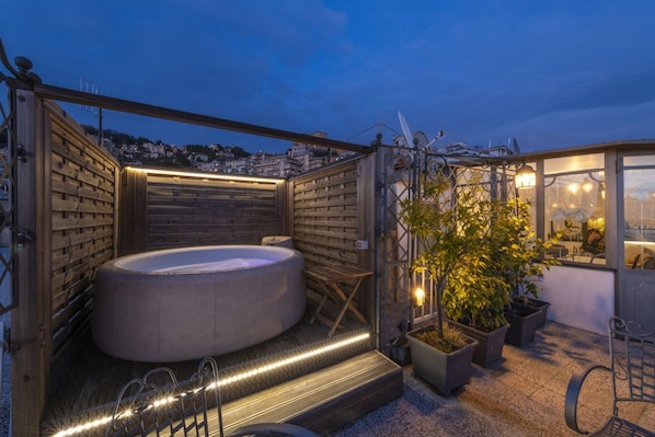 Eine Dachterrasse mit Whirlpool, Sitzgelegenheit, Topfpflanzen und Blick auf die Stadt.