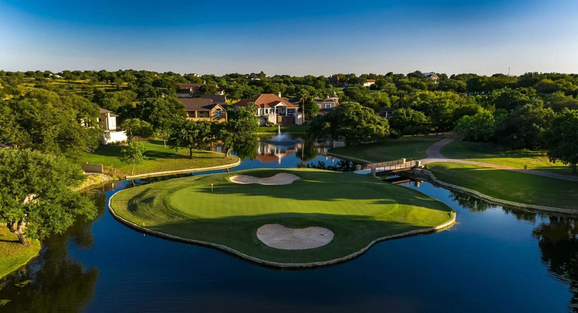 A golf course with a pond, surrounded by houses and trees.