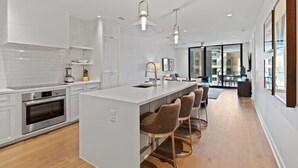 Una cucina moderna con mobili bianchi, un'isola centrale con sgabelli da bar e illuminazione a sospensione.