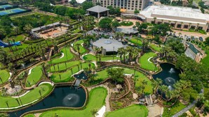 Una vista aerea di un campo da golf con più green, specchi d'acqua e edifici circostanti.