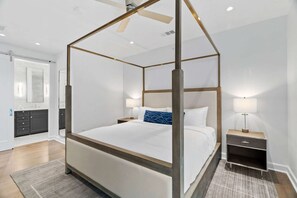 Uma cama de dossel com estrutura de madeira, uma mesa de cabeceira com luminária e um banheiro com espelho e toucador.